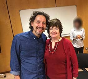 Lionel Vernois, hypnothérapeute, pose avec une femme souriante dans une salle, un homme en arrière-plan.