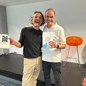 Lionel Vernois et un autre homme souriants, chacun tenant un livre sur une scène intérieure.
